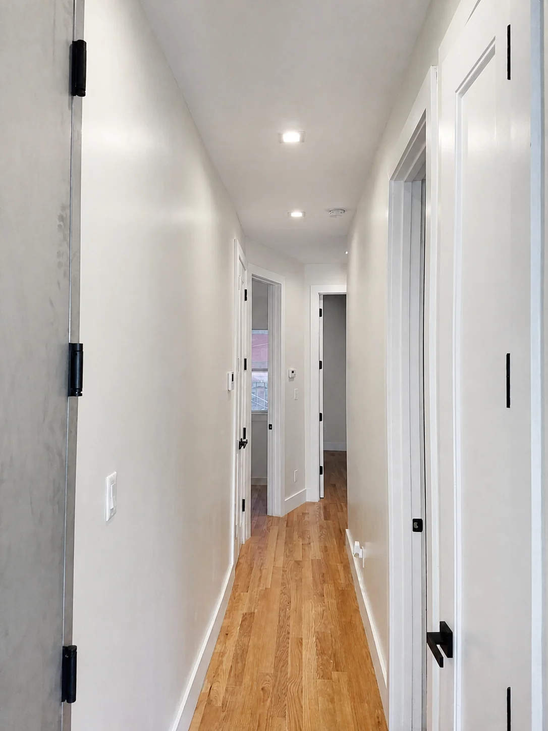 Finished hallway with painted walls, white door casing, baseboards and dark hardware