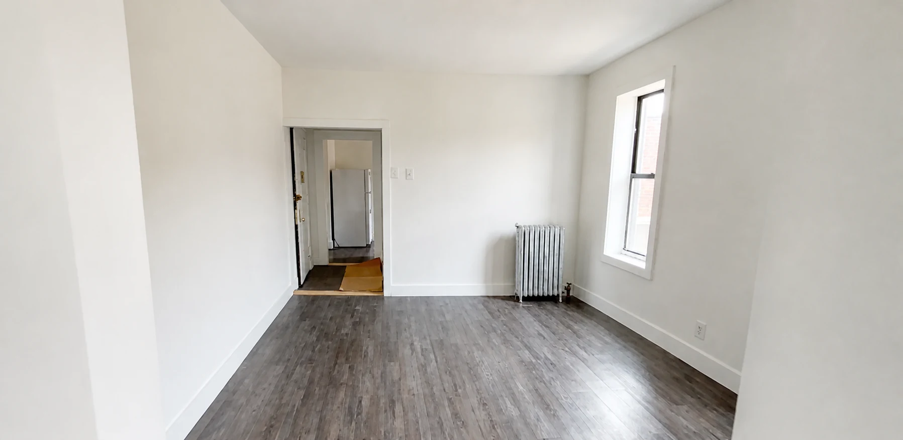 Finished room with dark laminate flooring, white walls and a window with radiator
