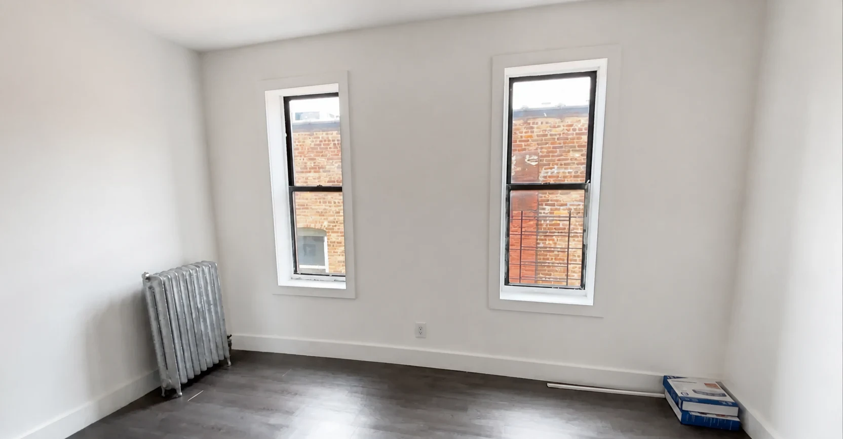 Finished room with dark laminate flooring, white walls and two windows